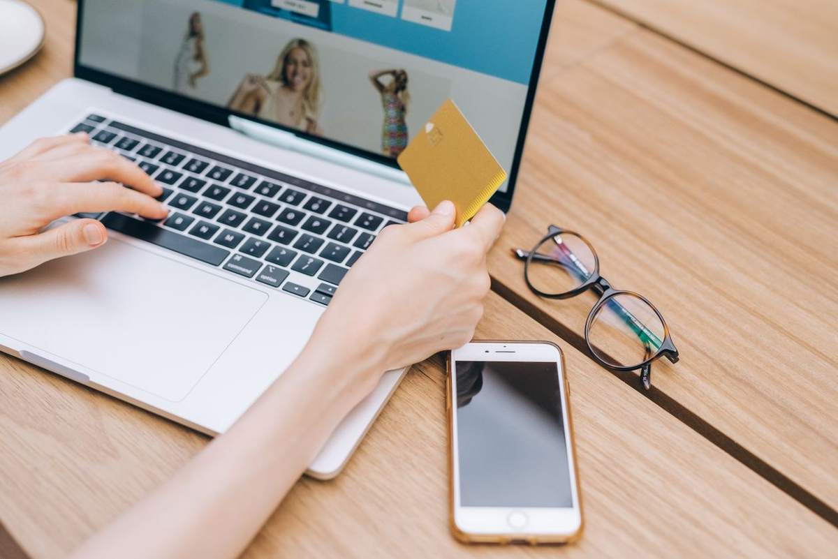 Person paying online with a credit card at a laptop, with a phone beside them