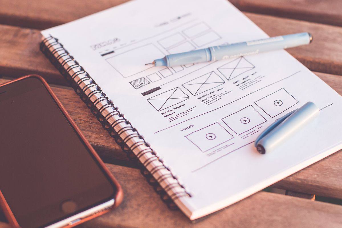 Website wireframe sketches in a notebook next to a phone